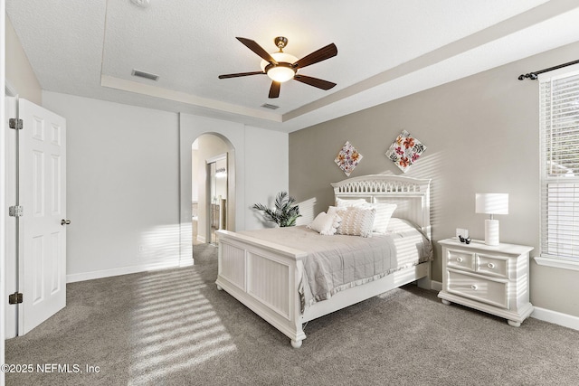 carpeted bedroom with visible vents, arched walkways, and a tray ceiling