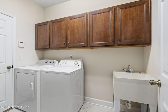 clothes washing area featuring a sink, cabinet space, independent washer and dryer, light tile patterned floors, and baseboards