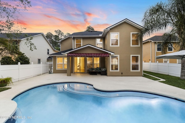 back of house at dusk with a fenced backyard, stucco siding, a fenced in pool, and a patio area