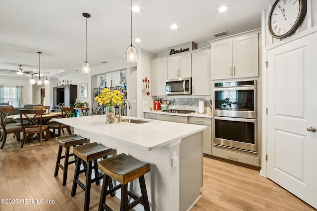 kitchen featuring decorative backsplash, light countertops, stainless steel appliances, an island with sink, and light wood-style floors