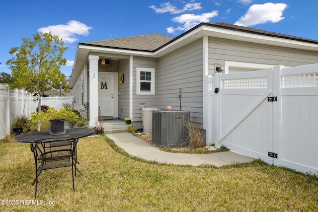 exterior space featuring cooling unit, roof with shingles, fence, a gate, and a yard