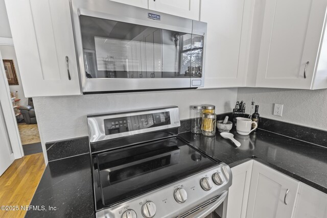 4 Pamela Pkwy, Palm Coast, FL 32137 - kitchen featuring wood finished floors, appliances with stainless steel finishes, dark stone countertops, white cabinetry, and a textured wall