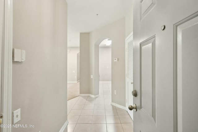 hallway featuring light tile patterned floors, baseboards, and arched walkways