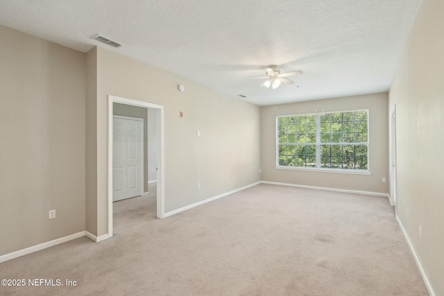 carpeted empty room featuring a textured ceiling, baseboards, a ceiling fan, and visible vents