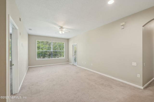 spare room featuring ceiling fan, carpet, arched walkways, a textured ceiling, and baseboards