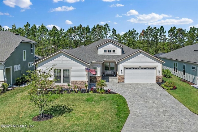 craftsman-style home featuring an attached garage, decorative driveway, a front lawn, and stone siding