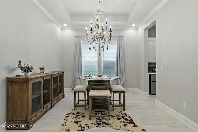 dining space with an inviting chandelier, ornamental molding, baseboards, light wood-type flooring, and a raised ceiling