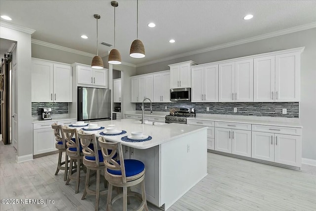 kitchen with light wood-style floors, a center island with sink, light countertops, tasteful backsplash, and stainless steel appliances