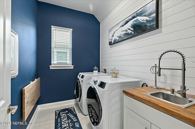 washroom with independent washer and dryer, wood walls, cabinet space, a sink, and baseboards