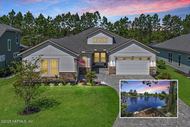 view of front of property featuring driveway, roof with shingles, a garage, a front lawn, and stone siding