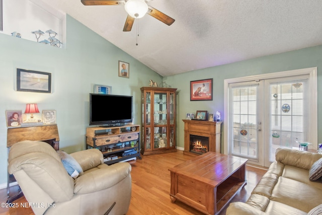 living room with a warm lit fireplace, vaulted ceiling, a textured ceiling, light wood-style floors, and a ceiling fan