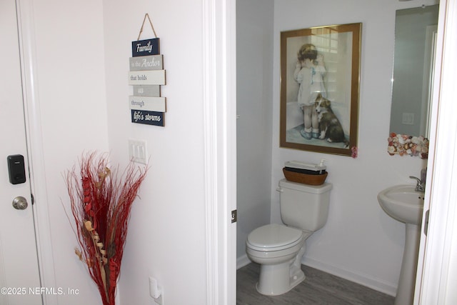 half bath with toilet, a sink, baseboards, and wood finished floors
