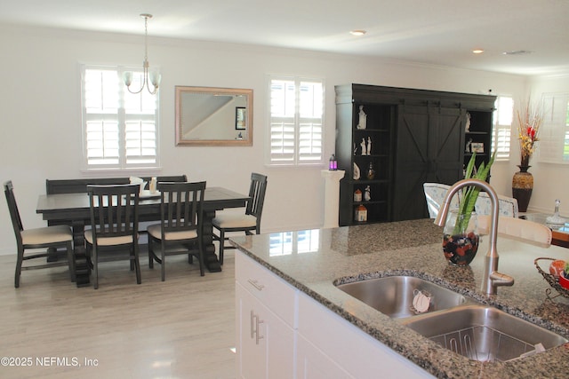 kitchen featuring decorative light fixtures, a sink, stone counters, light wood-style floors, and white cabinets