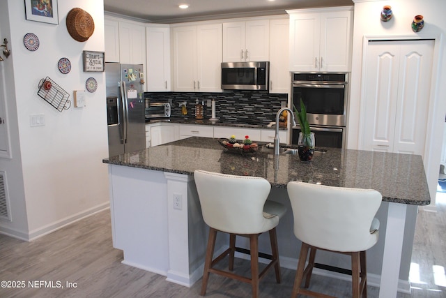 kitchen with appliances with stainless steel finishes, white cabinetry, a sink, light wood-type flooring, and backsplash