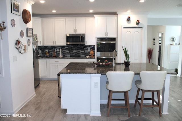 kitchen with decorative backsplash, light wood finished floors, appliances with stainless steel finishes, white cabinetry, and an island with sink