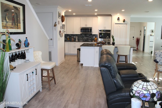 kitchen with crown molding, white cabinetry, light wood-style flooring, stainless steel appliances, and decorative backsplash