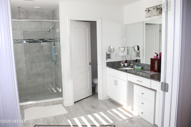 full bathroom with a stall shower, wood finished floors, toilet, and vanity