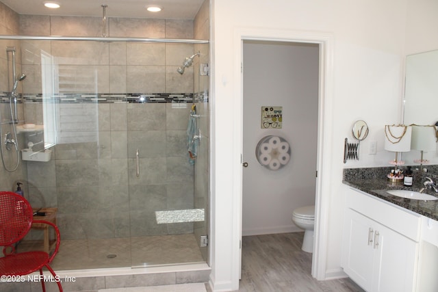 bathroom featuring toilet, vanity, a stall shower, and wood finished floors