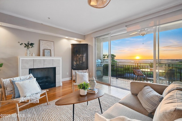 living area with a tile fireplace, baseboards, light wood-style flooring, and crown molding