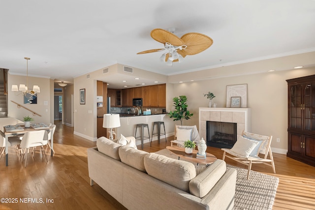 living room featuring light wood-style floors, a tile fireplace, visible vents, and ceiling fan with notable chandelier