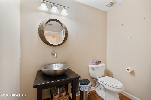 bathroom with wood finished floors, visible vents, toilet, a sink, and baseboards