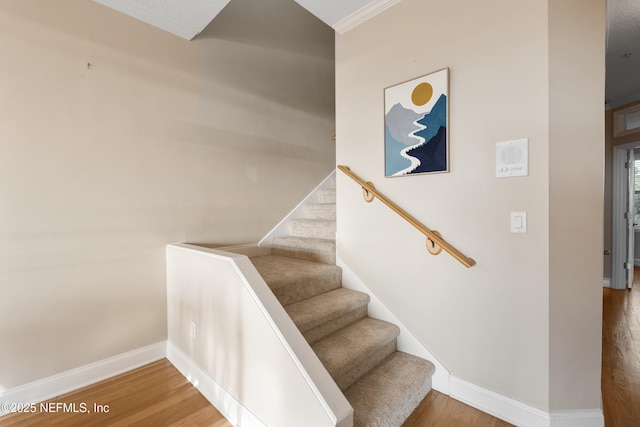 stairway with wood finished floors, baseboards, and ornamental molding