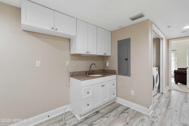 kitchen with a sink, electric panel, white cabinets, washer / clothes dryer, and visible vents