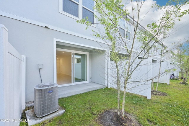 rear view of house with a lawn, cooling unit, and stucco siding
