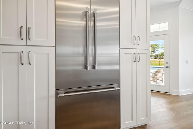 kitchen with crown molding, wood finished floors, baseboards, stainless steel built in refrigerator, and white cabinetry
