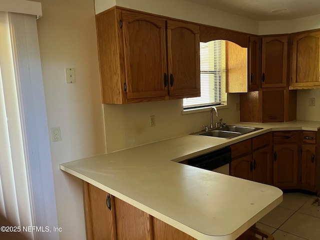 kitchen featuring light countertops, a peninsula, brown cabinetry, and a sink