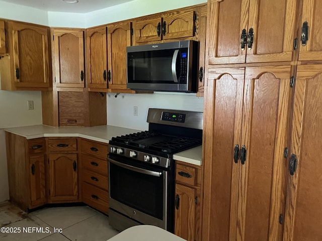 kitchen featuring brown cabinetry, light countertops, light tile patterned flooring, and stainless steel appliances