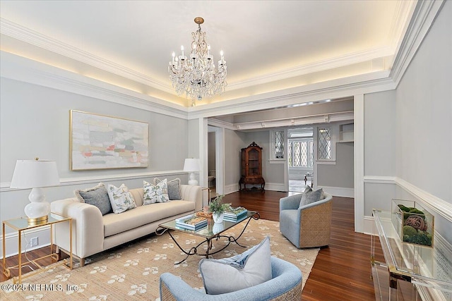living room with wood finished floors, a raised ceiling, ornamental molding, and an inviting chandelier