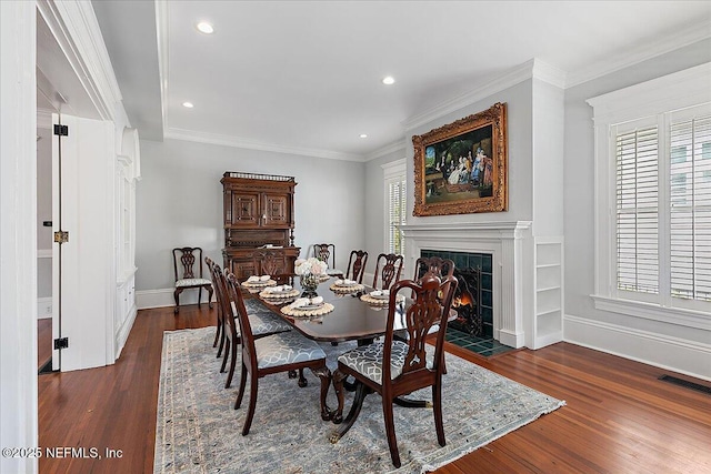dining space featuring crown molding, baseboards, visible vents, a tile fireplace, and wood finished floors