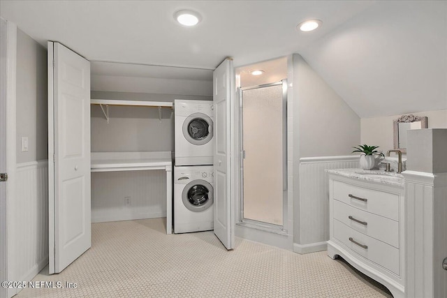 clothes washing area featuring wainscoting, recessed lighting, stacked washing maching and dryer, and a sink