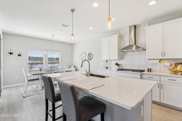 29 Stargaze Ln, Saint Augustine, FL 32095 - kitchen featuring wall chimney range hood, backsplash, an island with sink, white cabinetry, and stainless steel gas stovetop