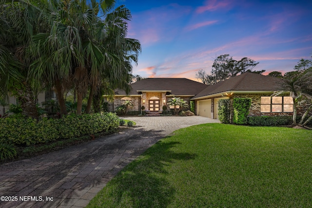 view of front facade featuring a lawn, decorative driveway, an attached garage, and brick siding