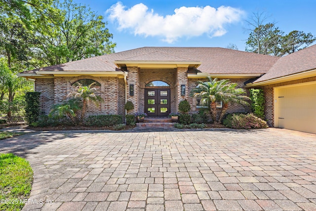view of front of home featuring brick siding, a garage, french doors, and decorative driveway