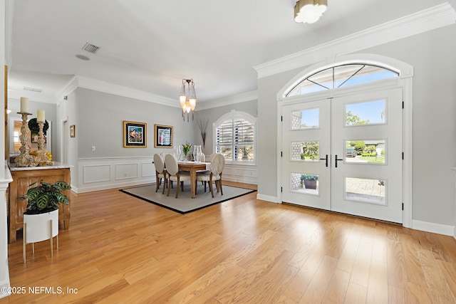 dining area with crown molding, french doors, light wood-type flooring, visible vents, and an inviting chandelier