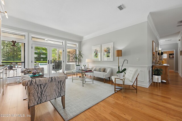 living area featuring french doors, ornamental molding, a wainscoted wall, light wood finished floors, and visible vents