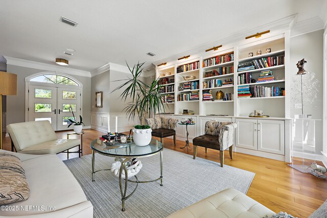 living area featuring a wainscoted wall, visible vents, crown molding, light wood finished floors, and french doors