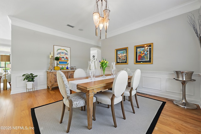dining area with light wood finished floors, visible vents, crown molding, and arched walkways
