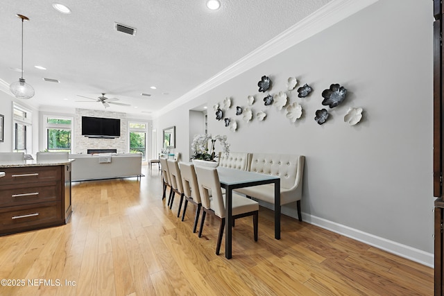 dining space featuring crown molding, a large fireplace, light wood-style flooring, visible vents, and ceiling fan