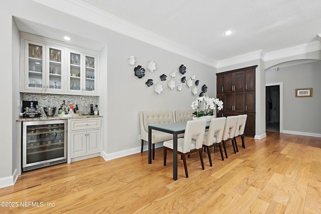dining area featuring a bar, light wood-type flooring, arched walkways, and beverage cooler