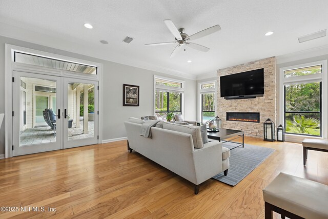 living room featuring crown molding, light wood finished floors, visible vents, a ceiling fan, and a stone fireplace