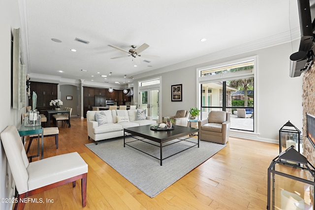 living area with ceiling fan, visible vents, ornamental molding, and light wood finished floors