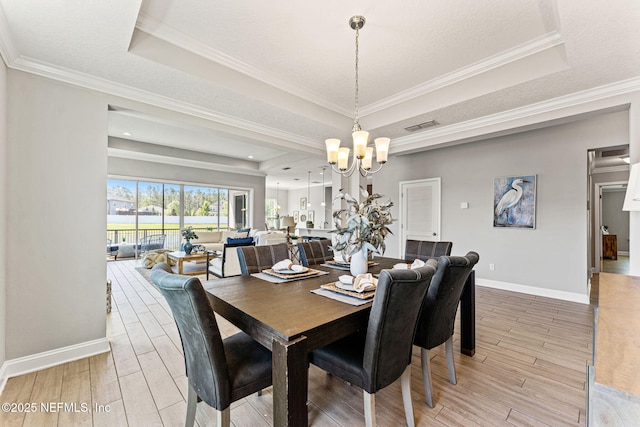 dining room with a chandelier, a tray ceiling, and light wood-style floors