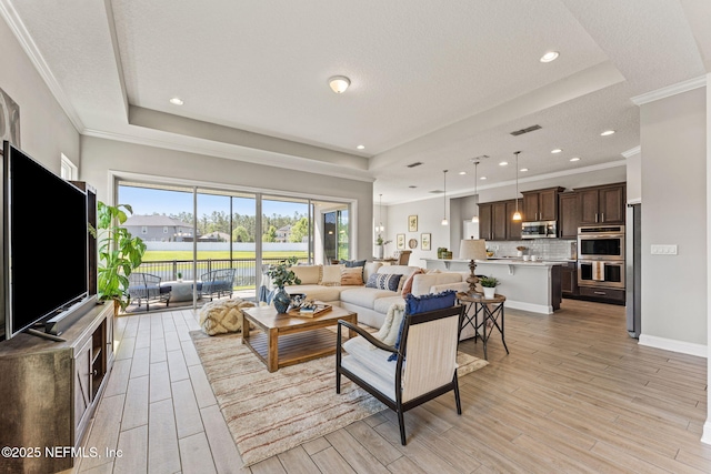 living area with ornamental molding, light wood finished floors, visible vents, and a raised ceiling