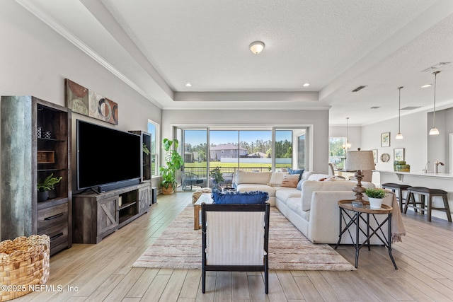 living area with a tray ceiling, visible vents, light wood-type flooring, crown molding, and a textured ceiling