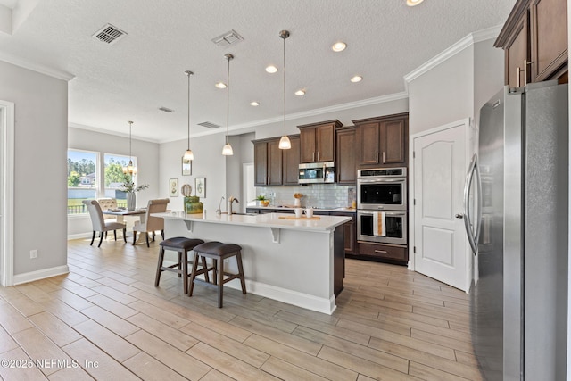 kitchen featuring a kitchen breakfast bar, light countertops, visible vents, a center island with sink, and appliances with stainless steel finishes