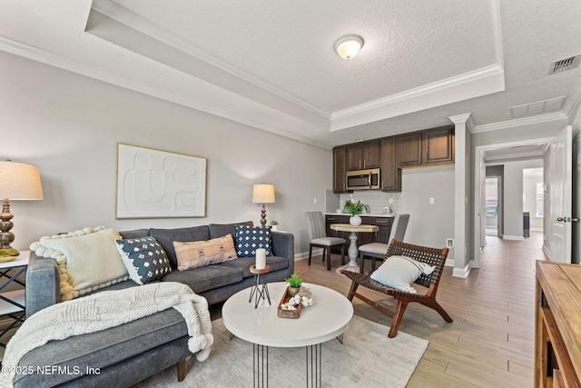 living room featuring visible vents, a tray ceiling, light wood finished floors, and ornamental molding
